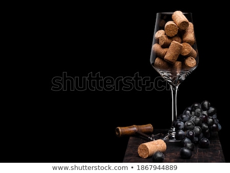 Imagine de stoc: Wine Glass With Corks Inside With Vintage Corkscrew Opener And Dark Grapes On Wooden Board On Black