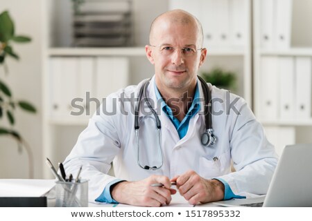 ストックフォト: Bald Professional Doctor With Pen Sitting By Desk In Medical Office Or Hospital