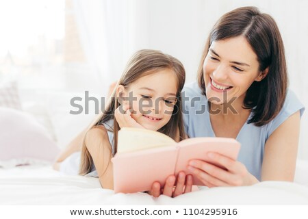 Stock photo: Pretty Female Mother And Her Small Daughter Read Interesting Book In Bedroom Lie On Comfortabled Be