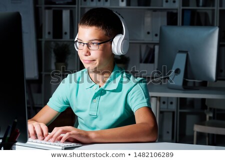 Stock foto: Clever Serious Schoolboy In Headphones Looking At Computer Screen In Darkness