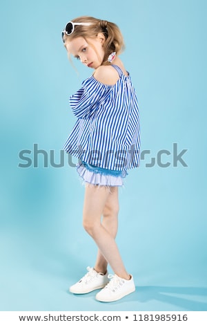 Stockfoto: A Girl In A T Shirt And Shorts With Glasses On Her Head Is Standing On A Blue Background