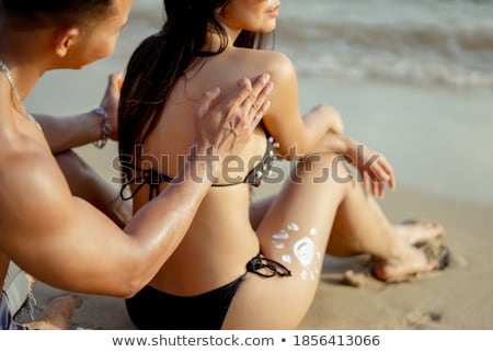 Stok fotoğraf: Woman Applying Spray On Man Back At Beach