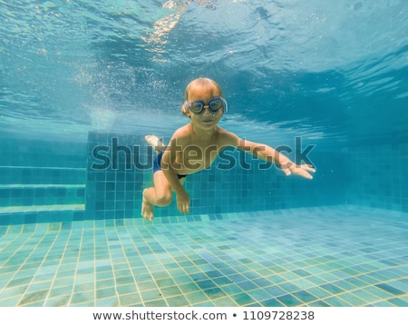 [[stock_photo]]: A Child Boy Is Swimming Underwater In A Pool Smiling And Holding Breath With Swimming Glasses