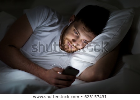 [[stock_photo]]: Man With Smartphone And Earphones In Bed At Night