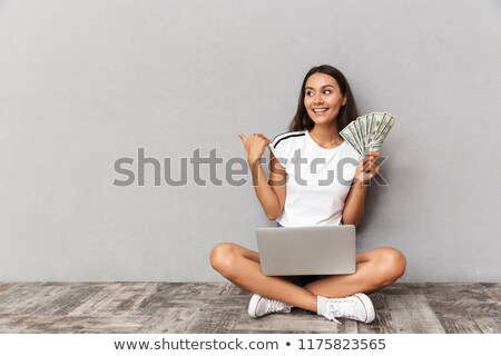 Сток-фото: Young Woman Sitting Isolated Over Grey Background Using Laptop Computer Holding Money Looking Aside