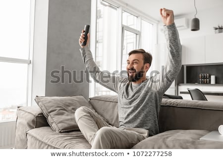 Foto d'archivio: Portrait Of A Cheerful Young Man Holding Tv Remote Control