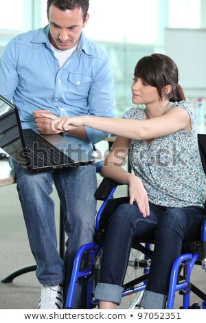 Foto stock: Young Woman In Wheelchair Being Shown Something On A Laptop Computer