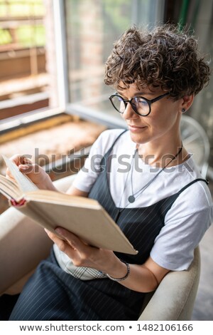 Foto d'archivio: Young Contemporary Woman Turning Page Of Interesting Book While Reading It