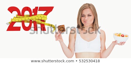 Stockfoto: Woman With Fruit Bowl Making Faces As She Looks At Cookie