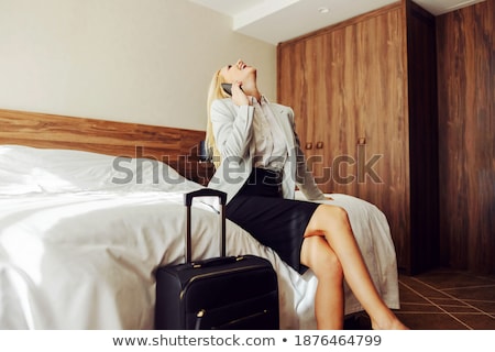 Foto stock: Woman Sitting On Hotel Bed Next To Her Suitcase