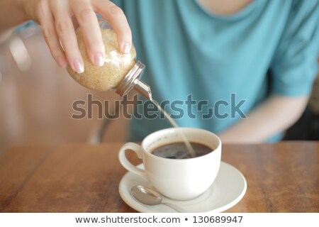 Stock photo: A Young Woman Sitting In A Cafe Pouring Sugar Into Her Tea