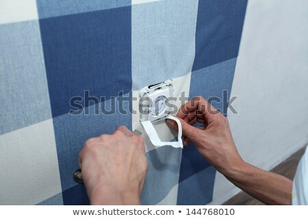 Foto d'archivio: Decorator With Scalpel Hanging Wallpaper Over Wall Socket