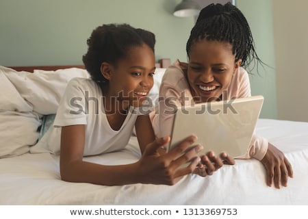 Stok fotoğraf: Front View Of Happy African American Mother And Daughter Lying On Bed And Using Digital Tablet In Be