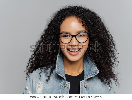 Stockfoto: Glad Woman With Curly Hair Wears Optical Glasses Denim Jacket Looks Straightly At Camera Isolate
