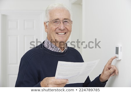 Zdjęcia stock: Smiling Senior Man With Bill Adjusting Central Heating Thermosta