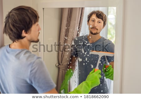 Stok fotoğraf: Young Man Cleaning Mirror At Home Hotel