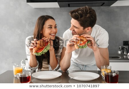 Foto d'archivio: Lovely Couple 30s Eating Sandwiches On Breakfast In Kitchen And