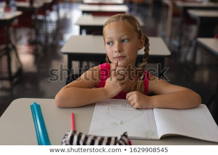Foto stock: Front View Of Thoughtful Schoolgirl Studying In Classroom Sitting At Desks In School