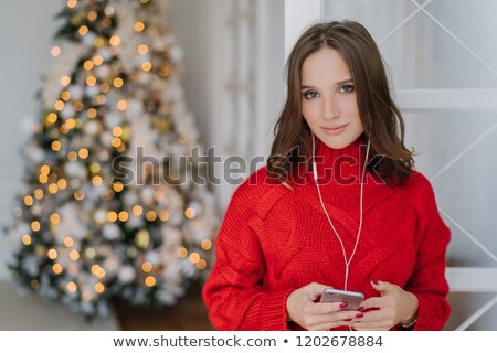 Stock fotó: Photo Of Cute Young Woman With Dark Hair Dressed In Knitted Red Sweater Holds Smart Phone In Hands