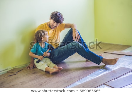 [[stock_photo]]: Father And Son Installing New Wooden Laminate Flooring Infrared Floor Heating System Under Laminate