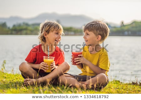 Foto d'archivio: Two Boys Drink Healthy Smoothies Against The Backdrop Of Palm Trees Mango And Watermelon Smoothies