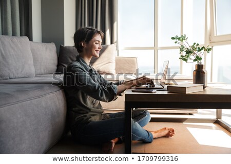 Stock fotó: Pleased Young Brunette Girl Sitting By The Table With Laptop