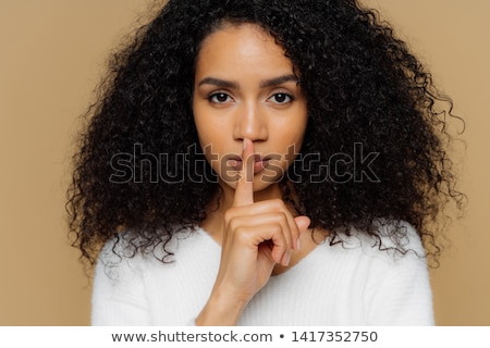 Foto d'archivio: Image Of Serious Confident Dark Skinned Woman Makes Shush Gesture Keeps Fore Finger Over Lips Tell