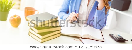 Foto d'archivio: Beautiful Young Girl Sitting At Desk In Office Holding A Pen In Her Hand And Reading A Book