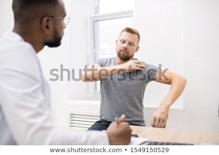 Stock photo: Young Sick Patient Touching His Shoulder While Showing Doctor Where It Hurts