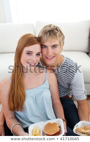 Foto stock: Teen Couple Eating Burgers And Fries On The Floor