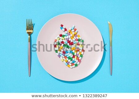 Foto stock: Colorful Capsules And Pills In The Form Of Fish On A Plate With Fork And Knife On A Blue Background