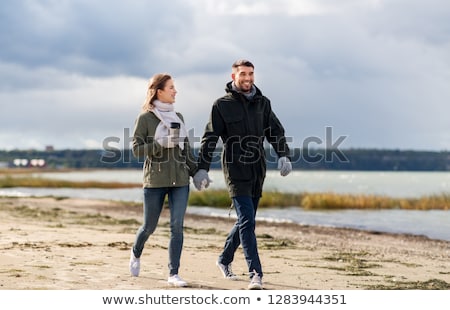 Stockfoto: Couple With Tumbler Walking Along Autumn Beach