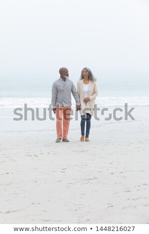 Foto stock: Front View Of Happy Senior Couple Holding Hands And Walking On Beach In The Sunshine