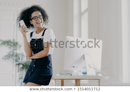 Foto stock: Happy Curly Haired Girl Uses Mobile Phone For Communication And Keeping In Touch Wears Spectacles A