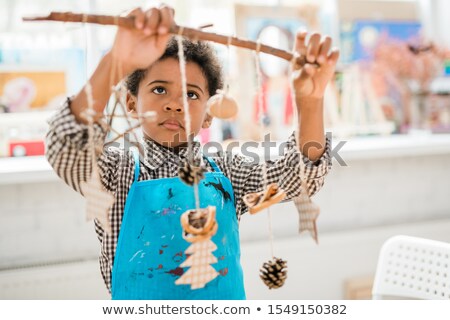 Foto stock: Cute Serious Schoolboy In Blue Apron Looking At Stick With Handmade Xmas Toys