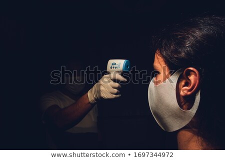 ストックフォト: Senior Medical Employee Measuring A Young Adults Body Temperature With Infrared Thermometer