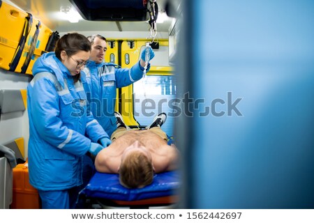 Сток-фото: Paramedic Examining Unconscious Shirtless Man While Colleague Holding Dropper