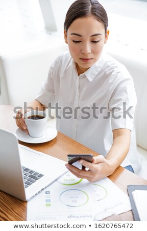 Foto stock: Beautiful Woman Holding Cup Of Coffee And Looking At Laptop