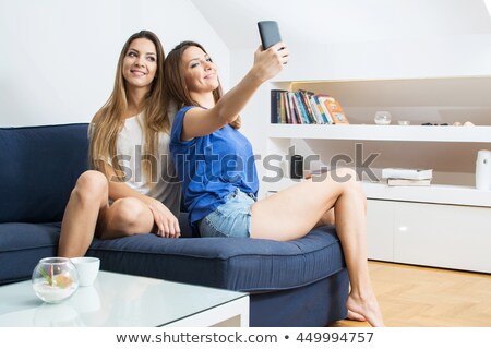 Stockfoto: Two Sisters Twins Sitting On Couch And Using Mobile Phones