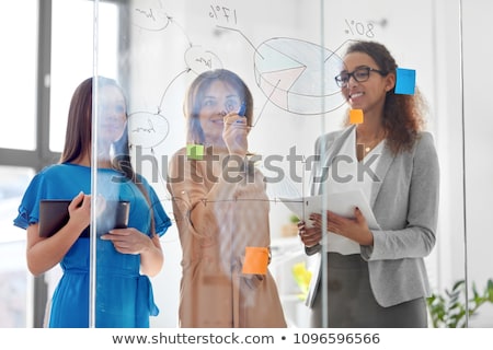 Stockfoto: Businesswomen With Pie Chart On Office Glass Board