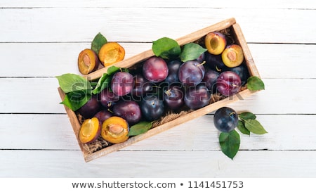 Foto d'archivio: Fresh Plums With Green Leaves On Wooden Rustic Background Top View