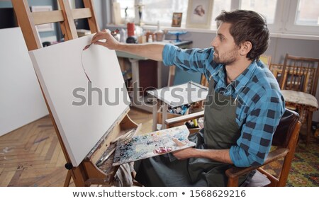 Foto stock: Serious Artist Concentrating On Painting New Masterpiece On Easel