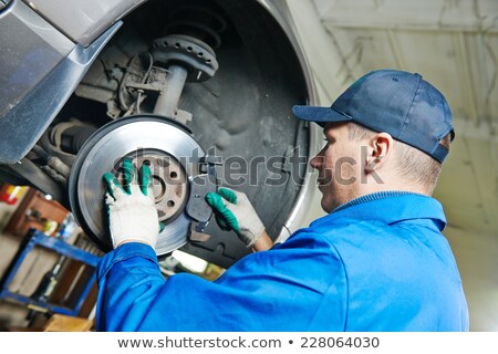 [[stock_photo]]: Mechanic Repairing Brake Of Lifted Automobile At Garage