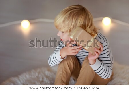 Foto d'archivio: A Blond Haired Boy Against The Background Of Luminous Light Bulbs Is Trying To Guess Which Gift Is I