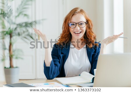 Stok fotoğraf: Shot Of Positive Red Haired Female Freelancer Works Remotely With Paper Documents Spreads Hands To
