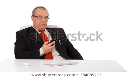 Сток-фото: Businessman Sitting At Desk And Holding A Mobilephone With Copys Pace Isolated On White