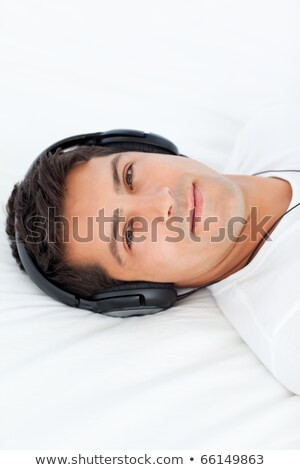Stockfoto: Serious Man With Headphones On Lying On His Bed At Home