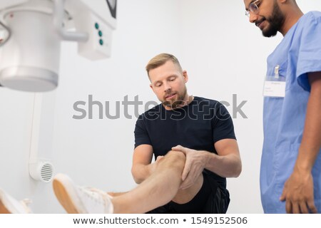 Stockfoto: Young Man Showing Sick Leg Or Knee While Describing His Problem To Doctor