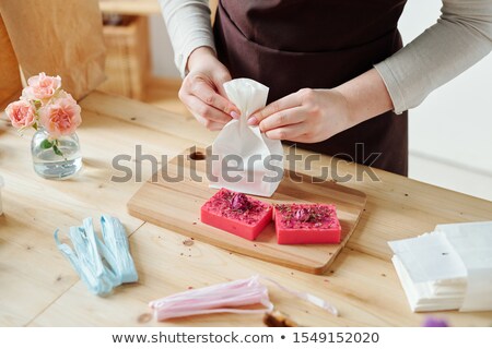 Stock foto: Hands Of Girl Packing Pink Handmade Soap Bar Into Paper Packet On Wooden Board