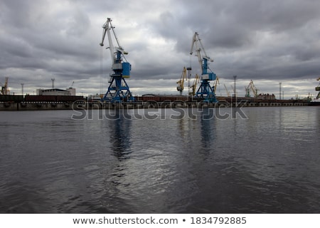 [[stock_photo]]: Sea Port Cranes With Blue Cloudy Sky In Background And Water In